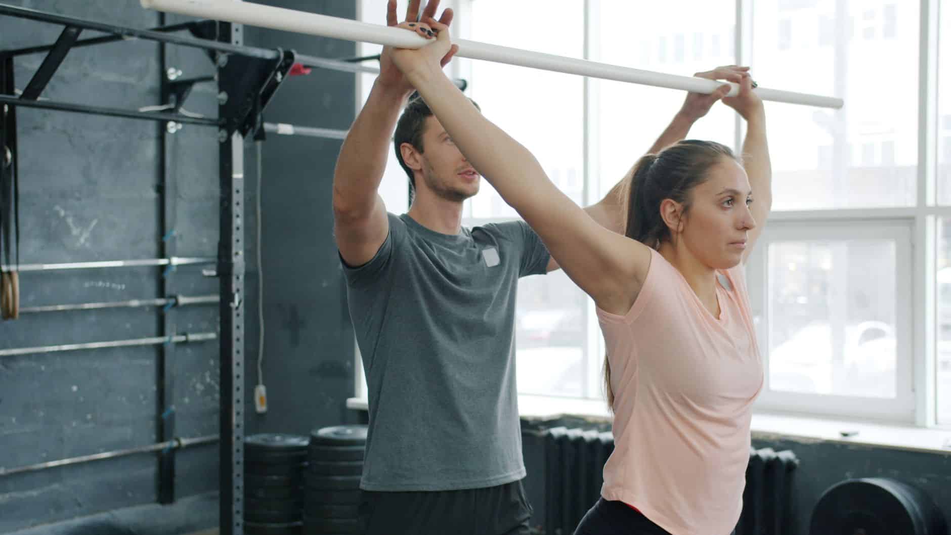 Home Personal trainer website: A personal trainer helps a woman with strength training exercises in the gym
