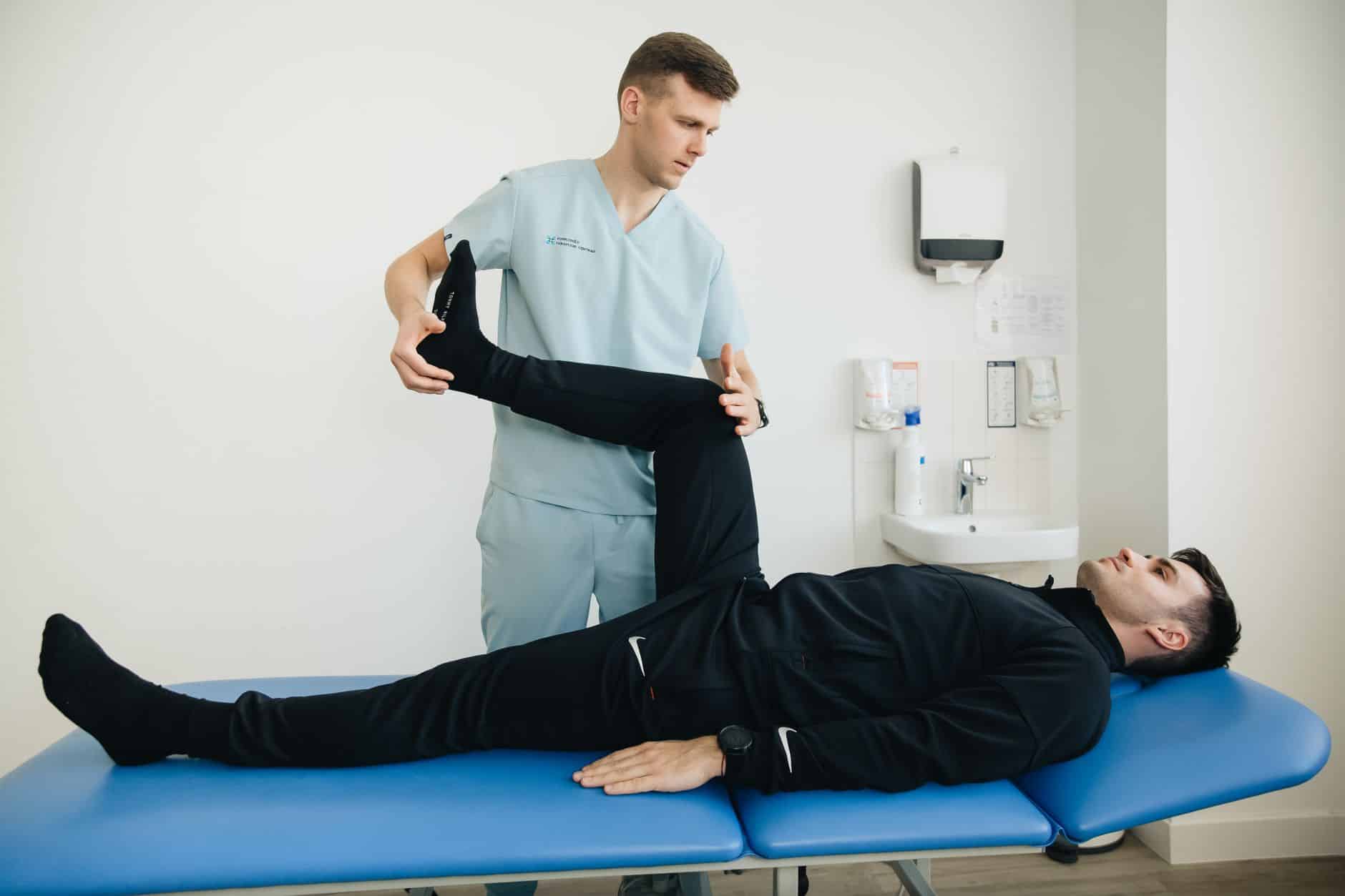 Home Starting a physiotherapy clinic: A physiotherapist assists a patient with leg stretching exercises on a treatment table